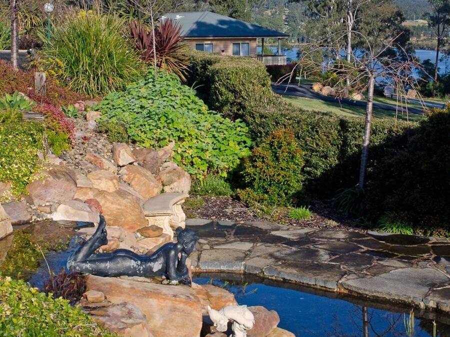 Un jardín ajardinado con un estanque, rocas y una casa al fondo.