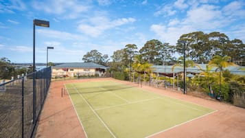 An outdoor tennis court with a net, surrounded by a fence and trees.