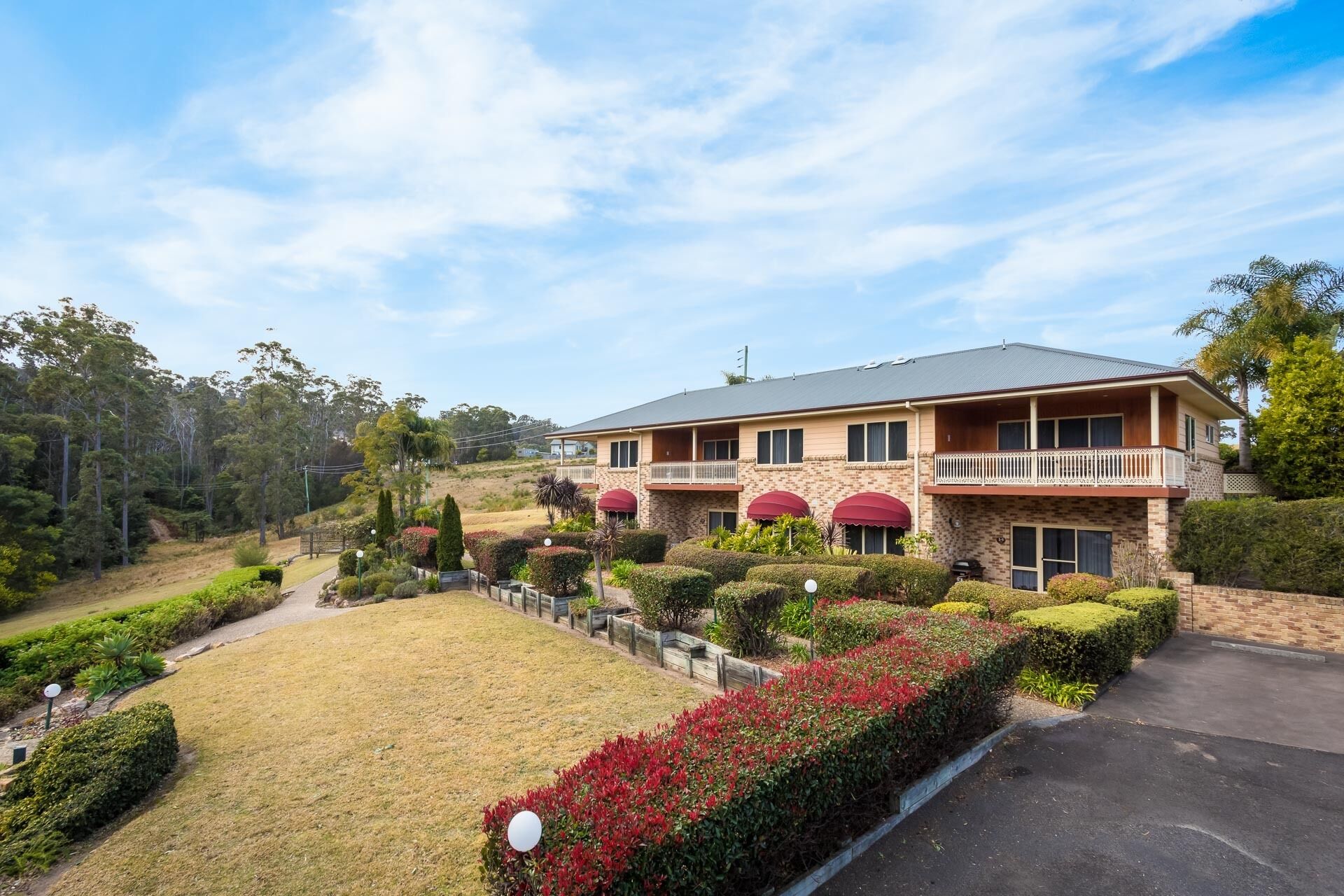 A two-story house with a balcony, surrounded by well-maintained gardens and a clear sky.