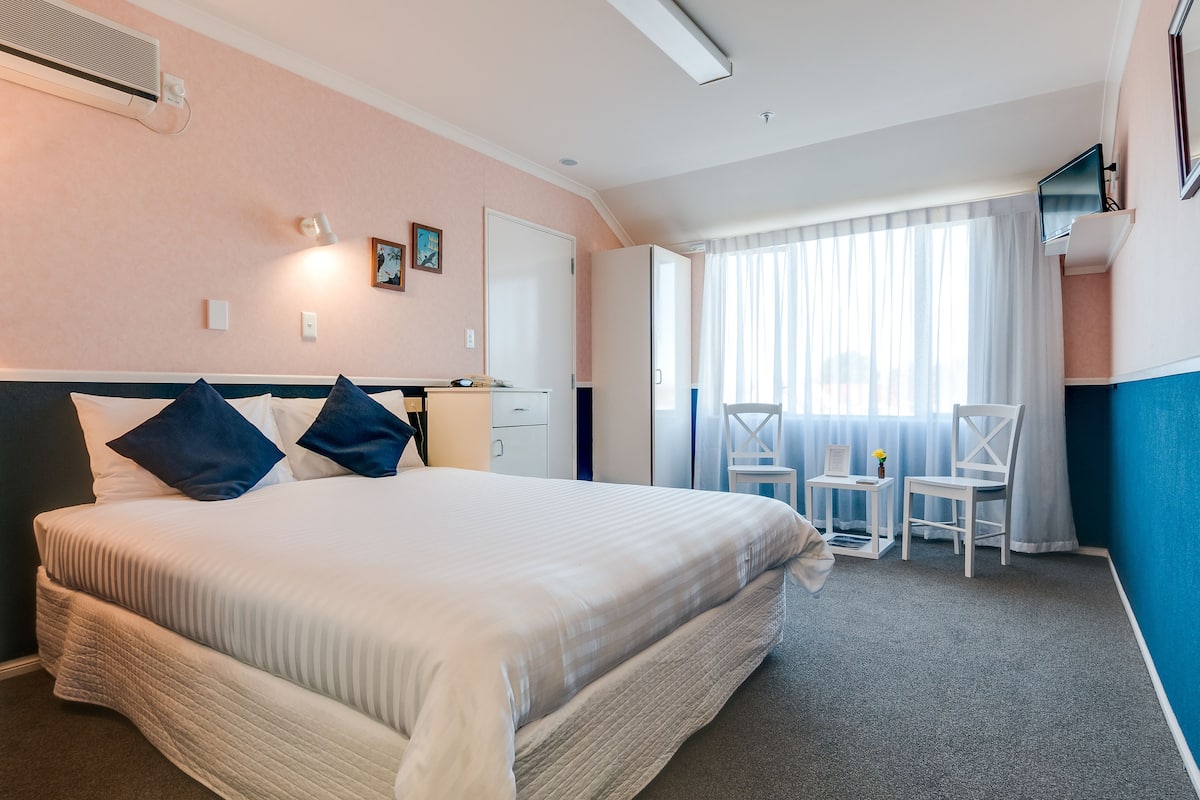 A hotel room with a large bed, a desk with a chair, a TV, and a window with curtains.