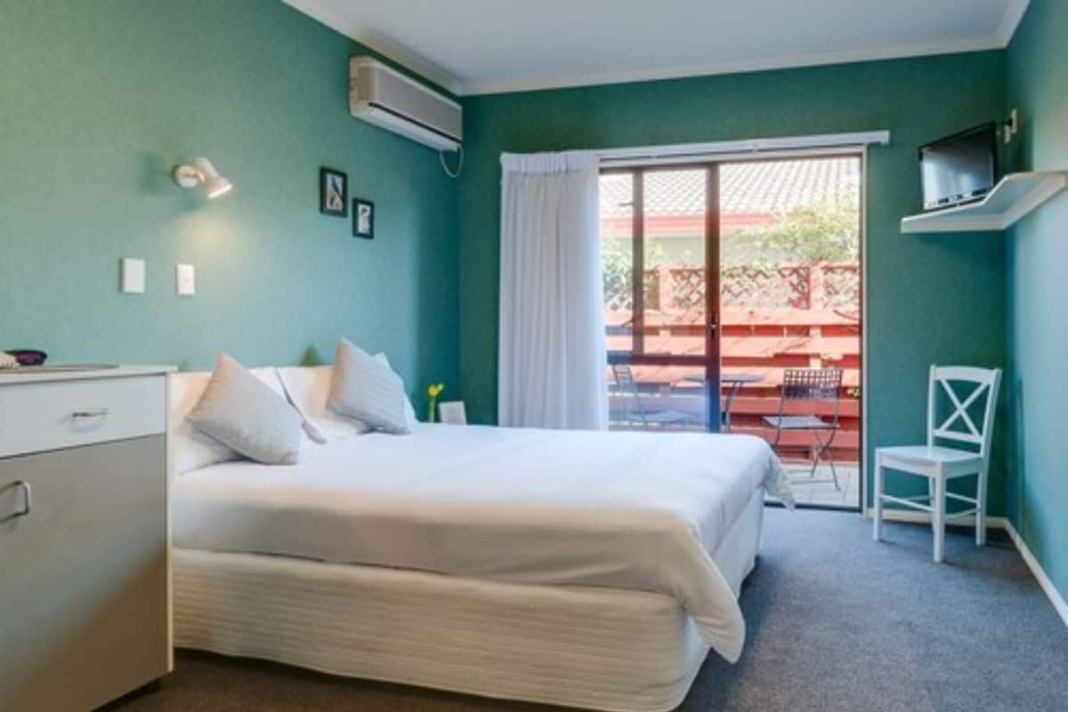 A bedroom with a bed, a desk, a chair, and a view of the outside.
