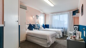 Ein Hotelzimmer mit zwei Betten, einem Schreibtisch mit Wasserkocher und einem fensterbepflanzten Fenster.