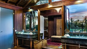 A bathroom with wooden beams, a large mirror, two sinks, and a view of palm trees. - Jeeva Saba Bali (Gianyar)