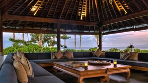 A spacious seating area with a view of the ocean, featuring a wooden coffee table and a sofa with cushions.