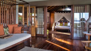A spacious bedroom with a wooden bed, a sitting area with a sofa, and a large window providing natural light. - Jeeva Saba Bali (Gianyar)