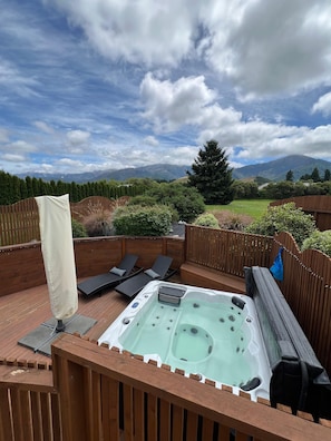 Ein Whirlpool auf einer Holzterrasse mit Liegestühlen und Blick auf Berge.