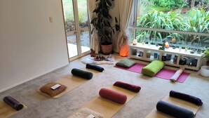 A yoga studio with mats and cushions arranged on the floor, a potted plant, and a view of greenery outside. - Vibrant Living Retreat (Hanmer Springs)