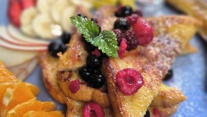A plate of French toast topped with berries and orange slices, accompanied by a small bowl of syrup and a side of fruit. - Vibrant Living Retreat (Hanmer Springs)