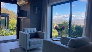A modern living room with a large window offering a scenic view of mountains and greenery. - Cape Vermeer (Cape Town)