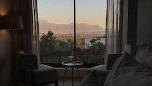 A bedroom with a large window, a bed, two chairs, a small table, and a lamp. - Cape Vermeer (Cape Town)