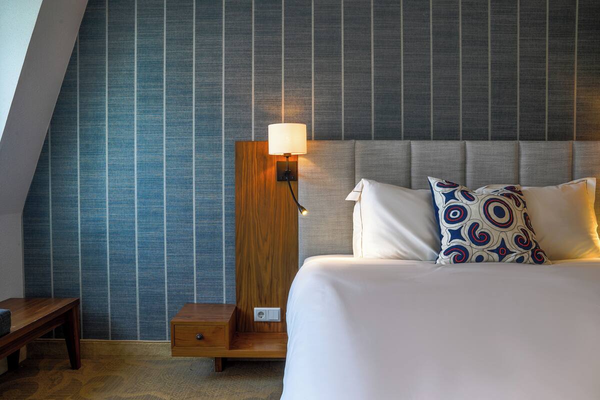 Ein Hotelzimmer mit einem großen Bett, einem Nachttisch, einer Wandlampe und einem gemusterten Kissen.