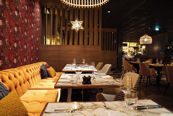 A restaurant with a wooden floor, a sofa, tables, and chairs. - Grand Hotel Ter Duin (Burgh-Haamstede)
