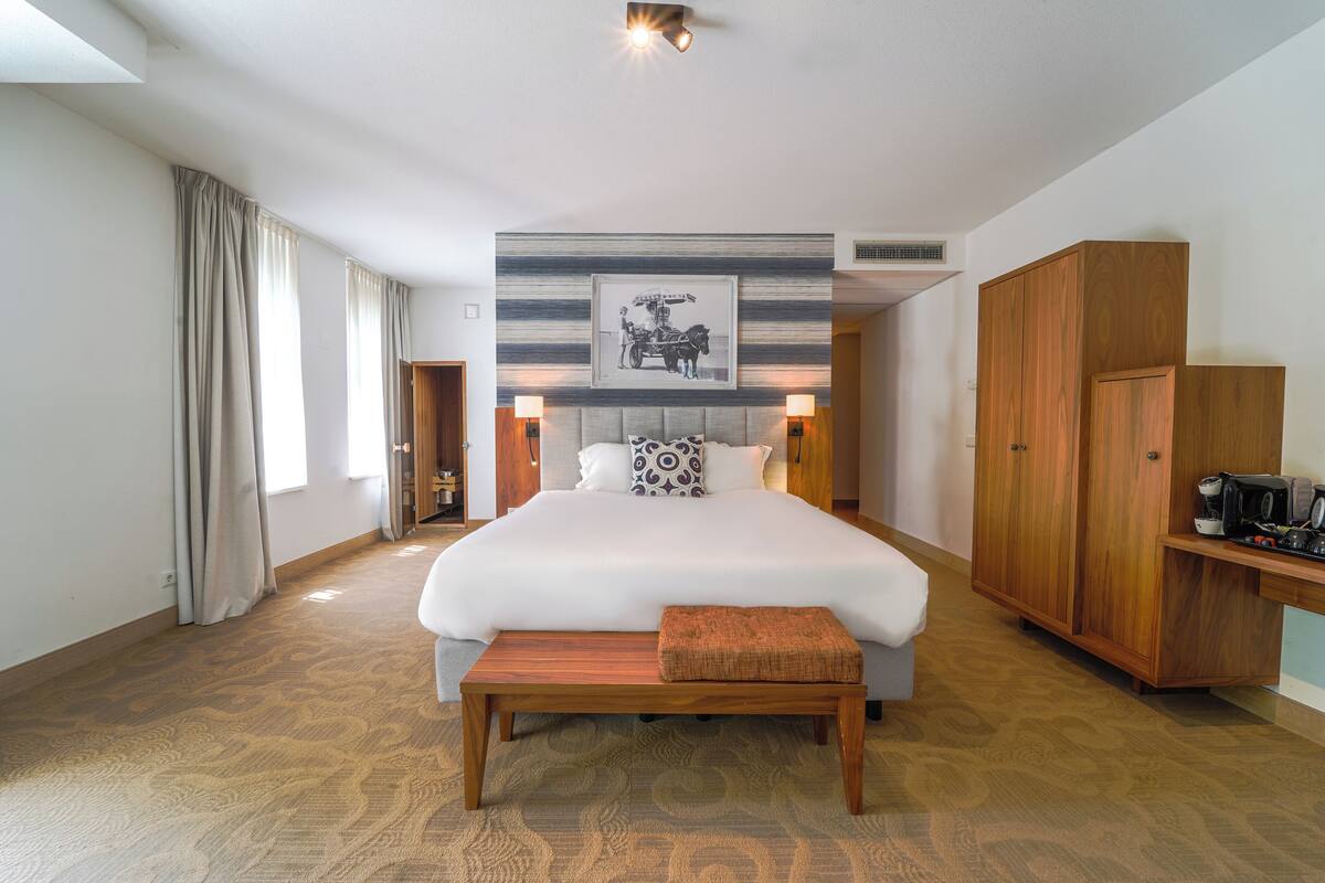 Ein Hotelzimmer mit einem großen Bett, einer Holzbank, einem Kleiderschrank und einem an der Wand hängenden Bild.