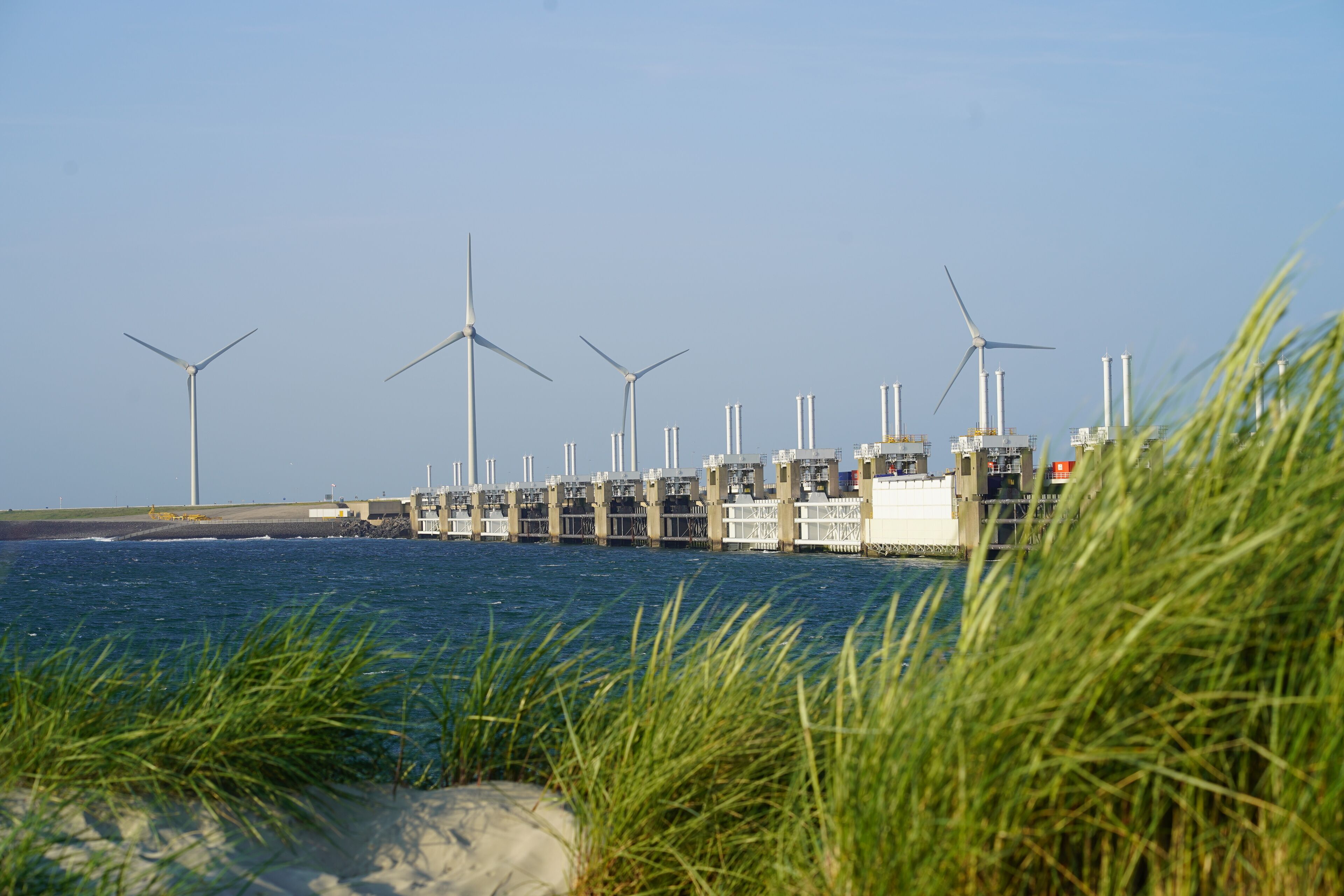 A coastal wind farm with multiple wind turbines and industrial structures by the sea.