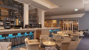 Uma área de bar moderna com cadeiras listradas, um balcão com banquetas e uma escadaria que leva a um andar superior.