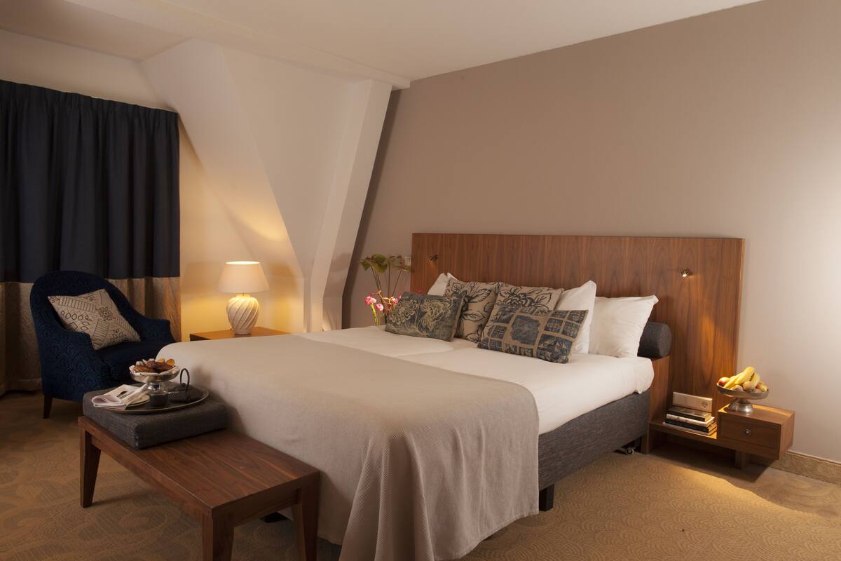 Ein Hotelzimmer mit einem großen Bett, einem Nachttisch, einem Sessel, einer Lampe und einem kleinen Tisch mit Tablett.