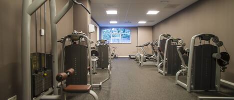 A gym with various exercise machines, a window with a view, and a carpeted floor.