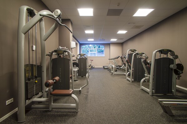A gym with various exercise machines, a window with a view, and a carpeted floor. - Grand Hotel Ter Duin (Burgh-Haamstede)