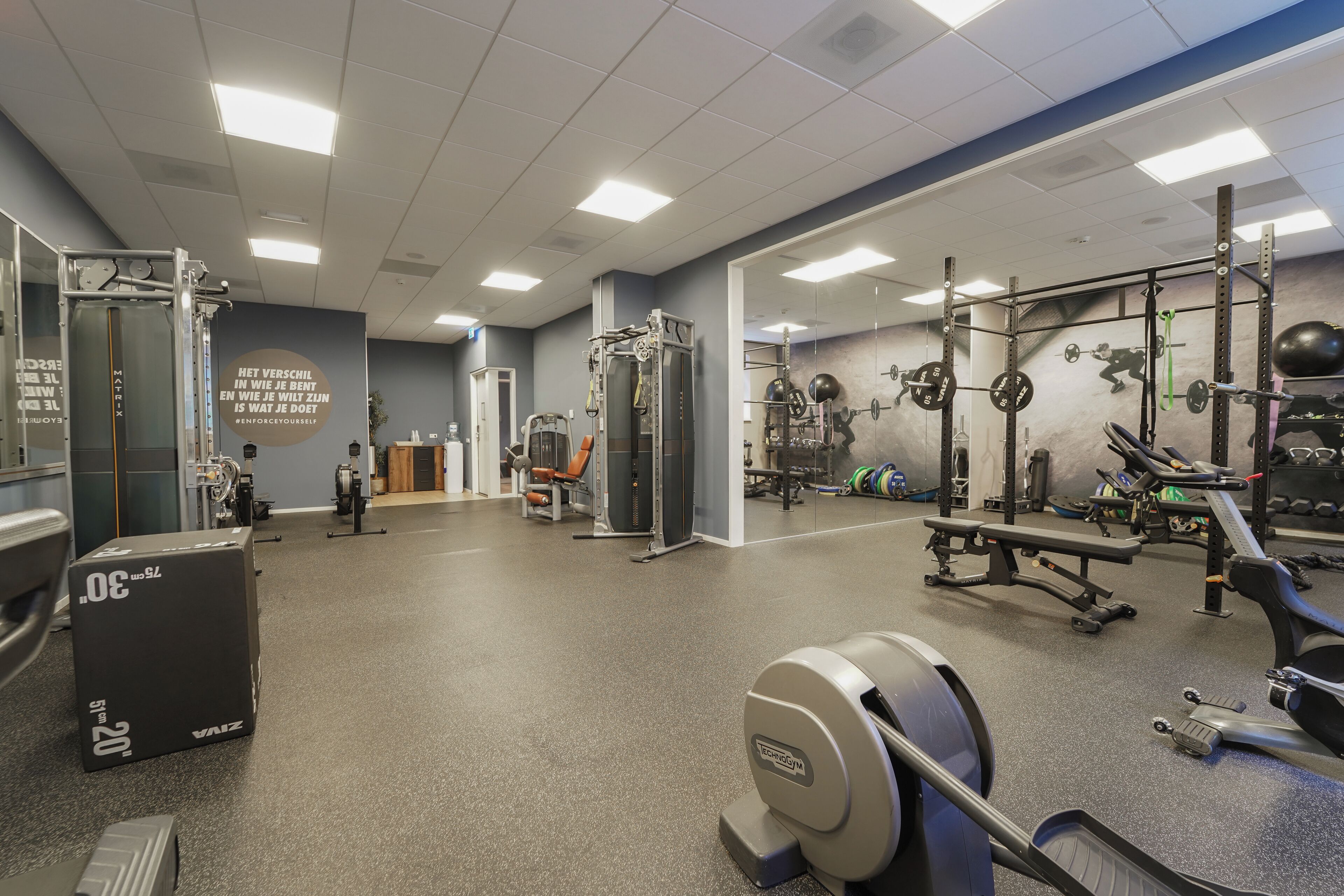 Un gimnasio con equipo de levantamiento de pesas, máquinas de cardio y un muro de espejos.