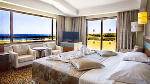 A hotel room with a bed, two armchairs, a small table, a TV, and large windows with a view of the sea. - Özkaymak Select Hotel - Ultra All Inclusive  (Alanya)