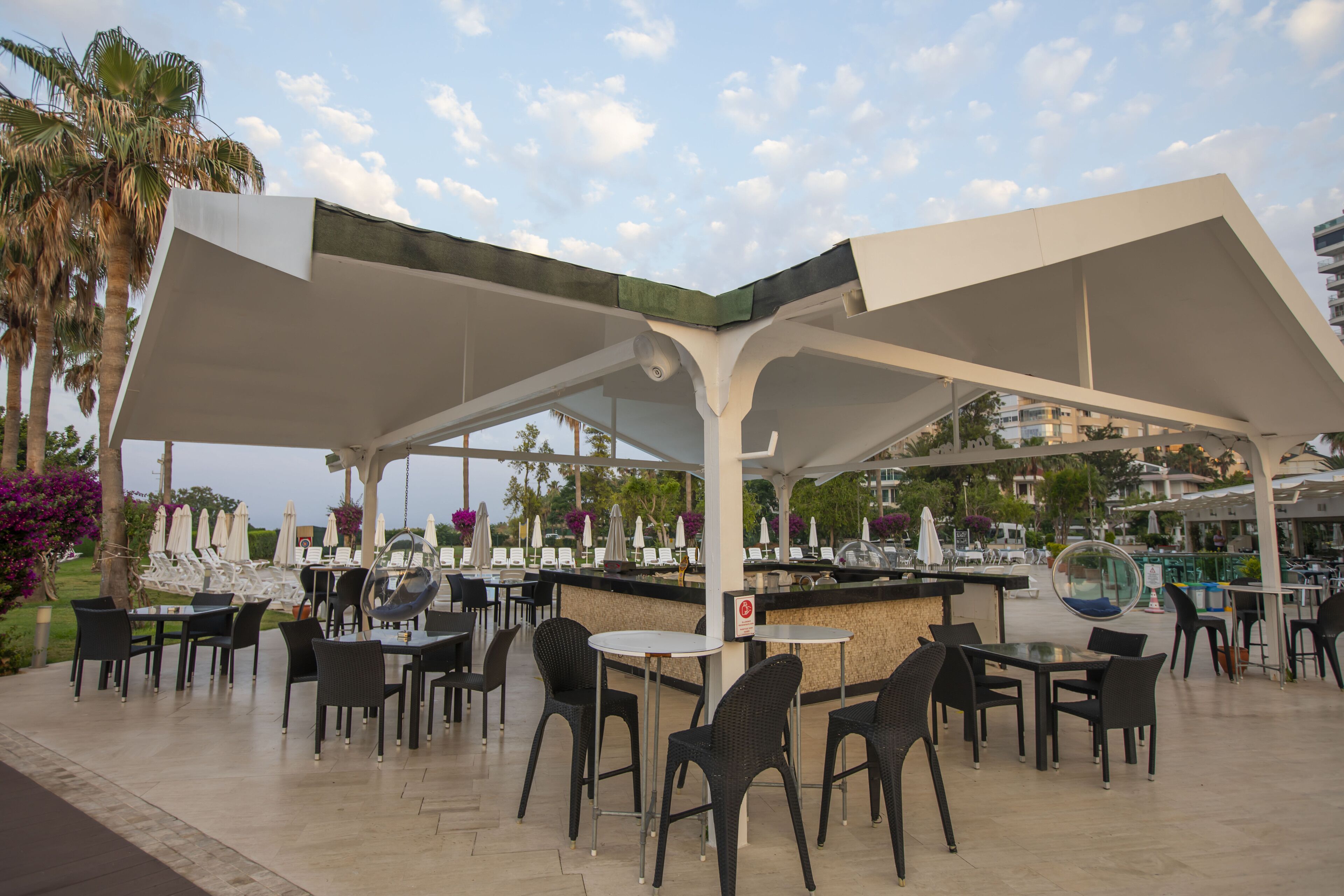 Een terras met tafels, stoelen, parasols en een bar.