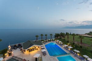 A resort with a large swimming pool, outdoor seating, and a view of the sea.