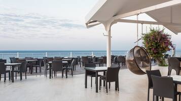 Un espace extérieur aménagé pour les repas, avec des tables et des chaises, offrant une vue sur la mer.