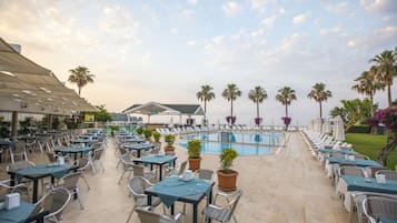 Un espacio al aire libre con mesas y sillas, una piscina y palmeras.