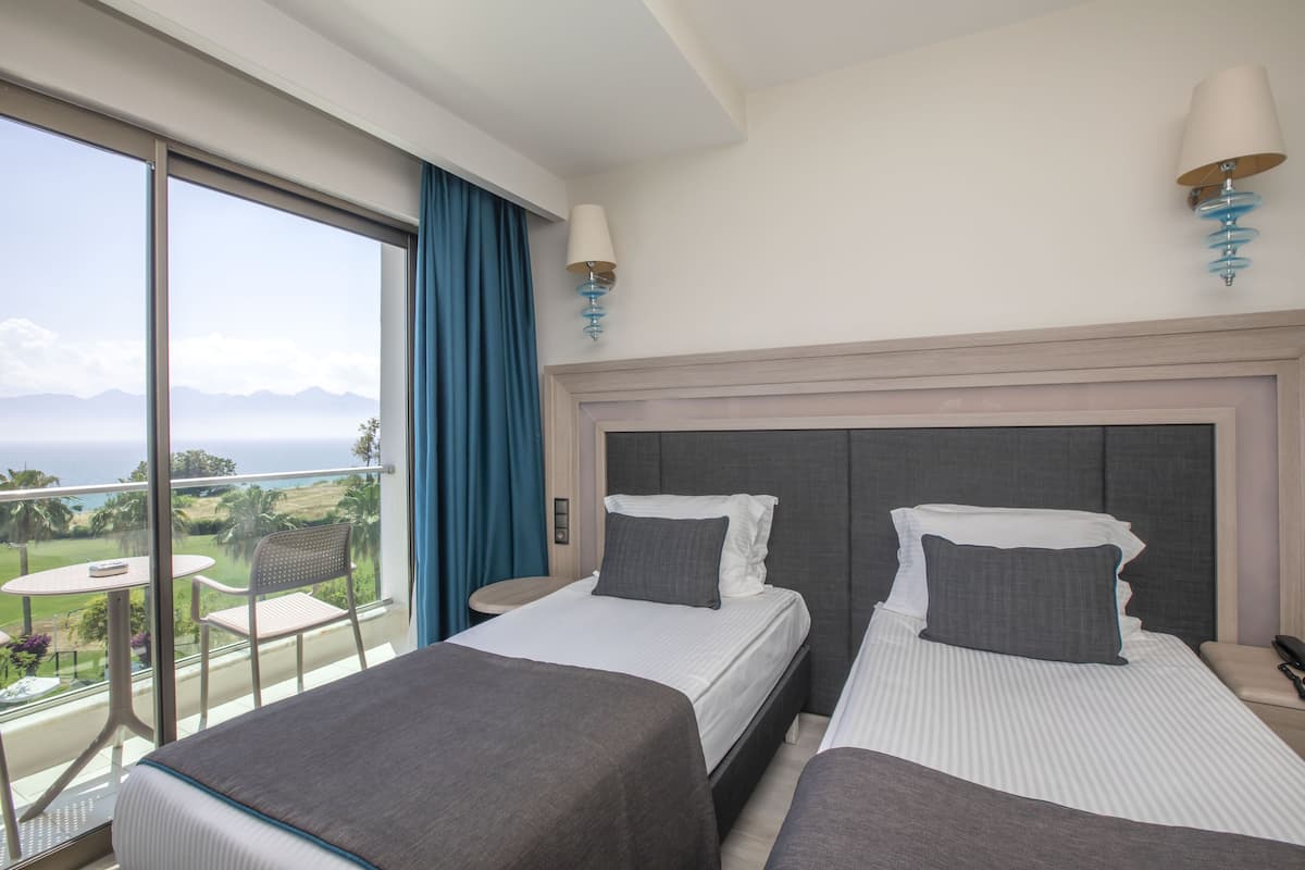 Ein Hotelzimmer mit zwei Betten, einem Balkon mit Tisch und Stühlen sowie Bergblick.