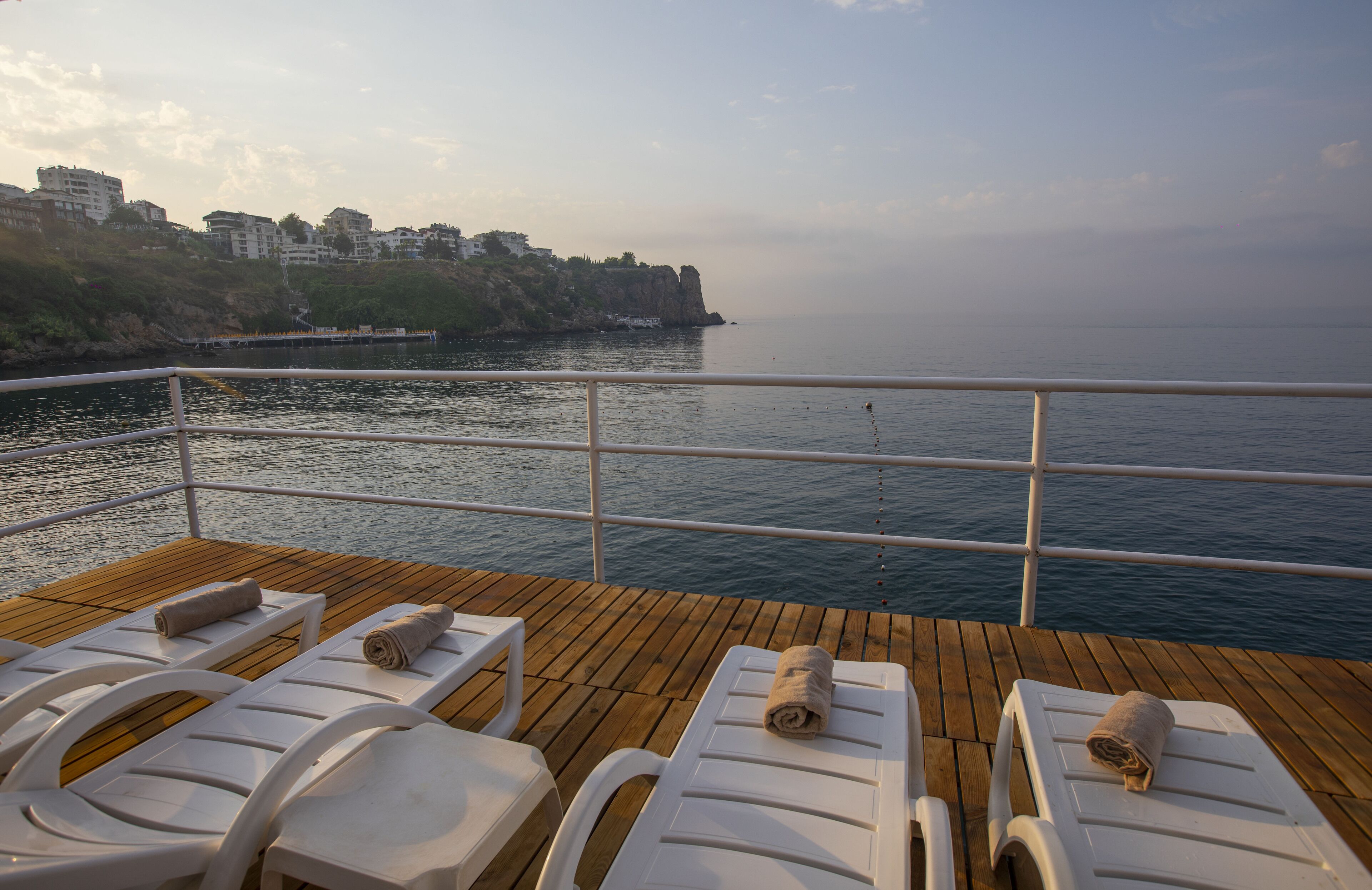 A deck with lounge chairs and a railing overlooking a body of water with buildings in the background.