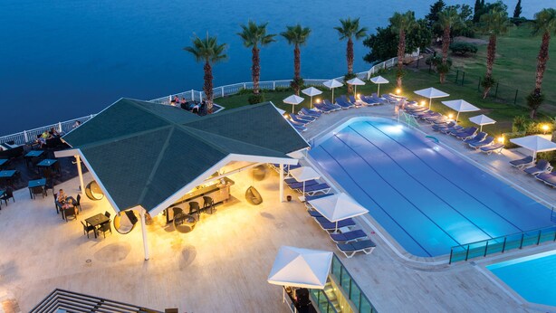 A rooftop pool area with lounge chairs and umbrellas, overlooking a body of water. - Falcon Hotel (Antalya)