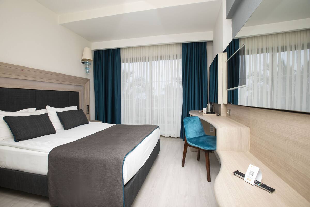 Ein Hotelzimmer mit einem Bett, einem Schreibtisch, einem Stuhl, einem Spiegel und einer Fernbedienung auf dem Schreibtisch.