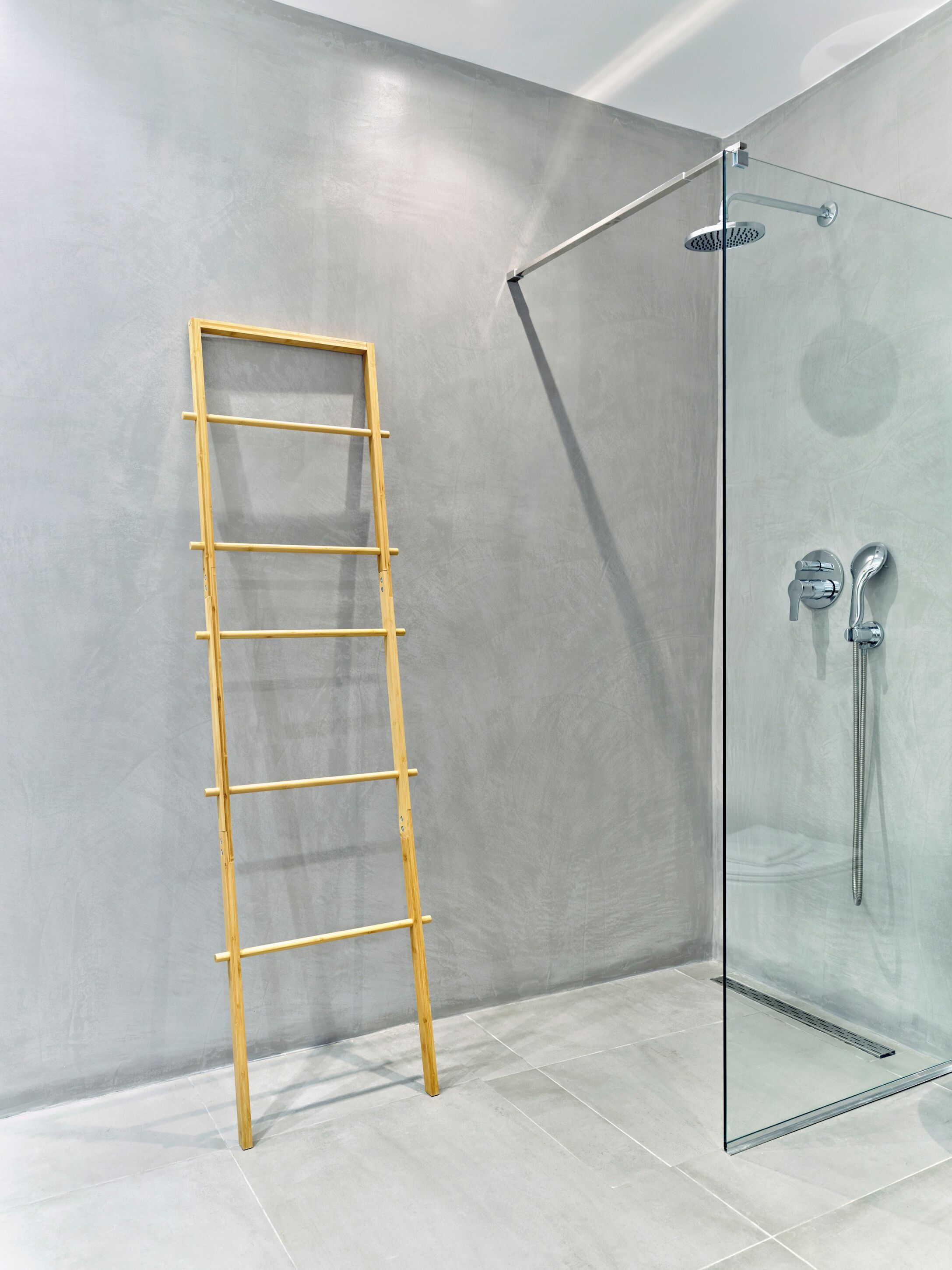 A modern bathroom with a glass shower enclosure, a wooden ladder, and a tiled floor.