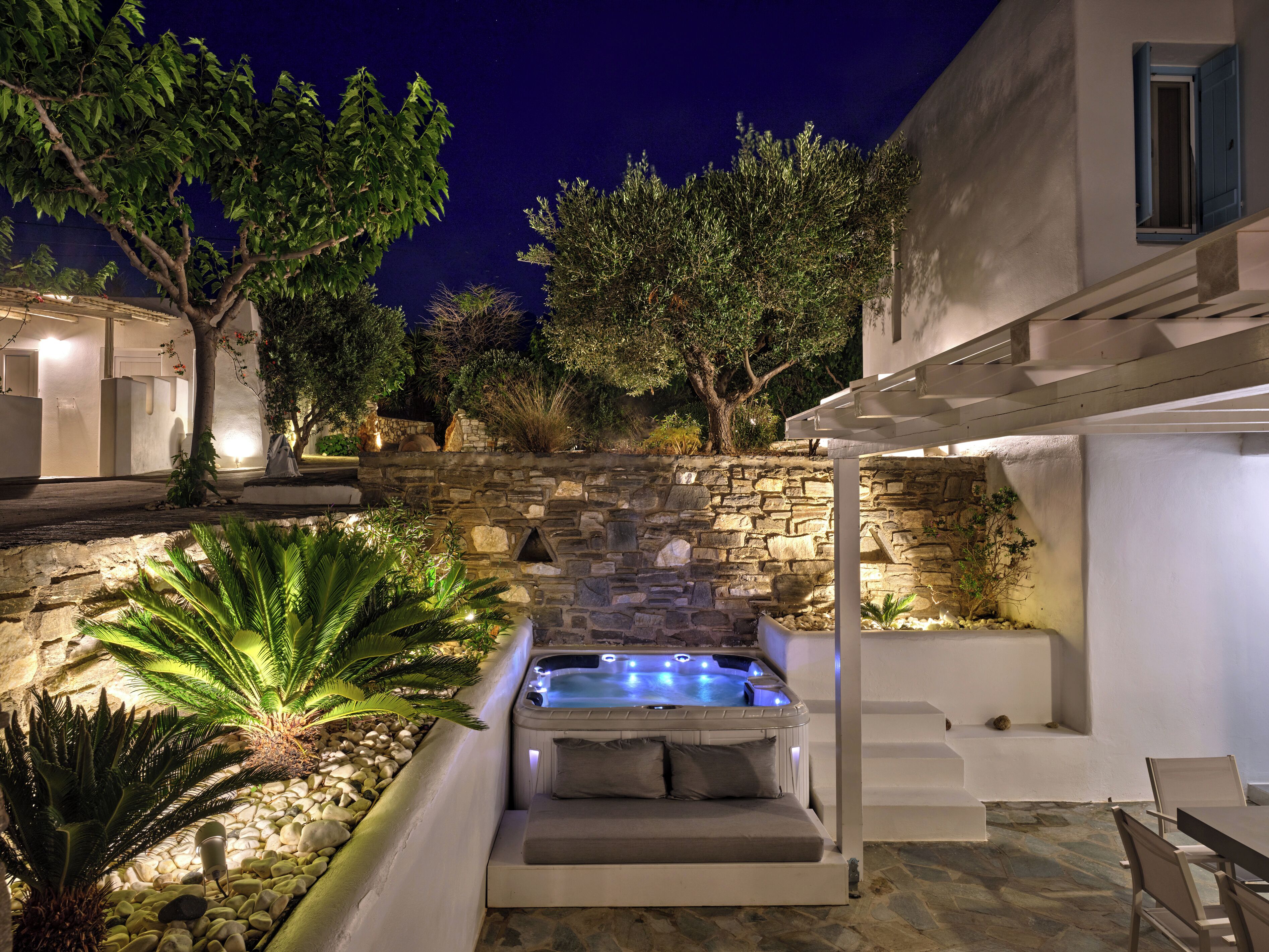 Pared de piedra con un jacuzzi y zona de estar, rodeado de plantas y árboles.