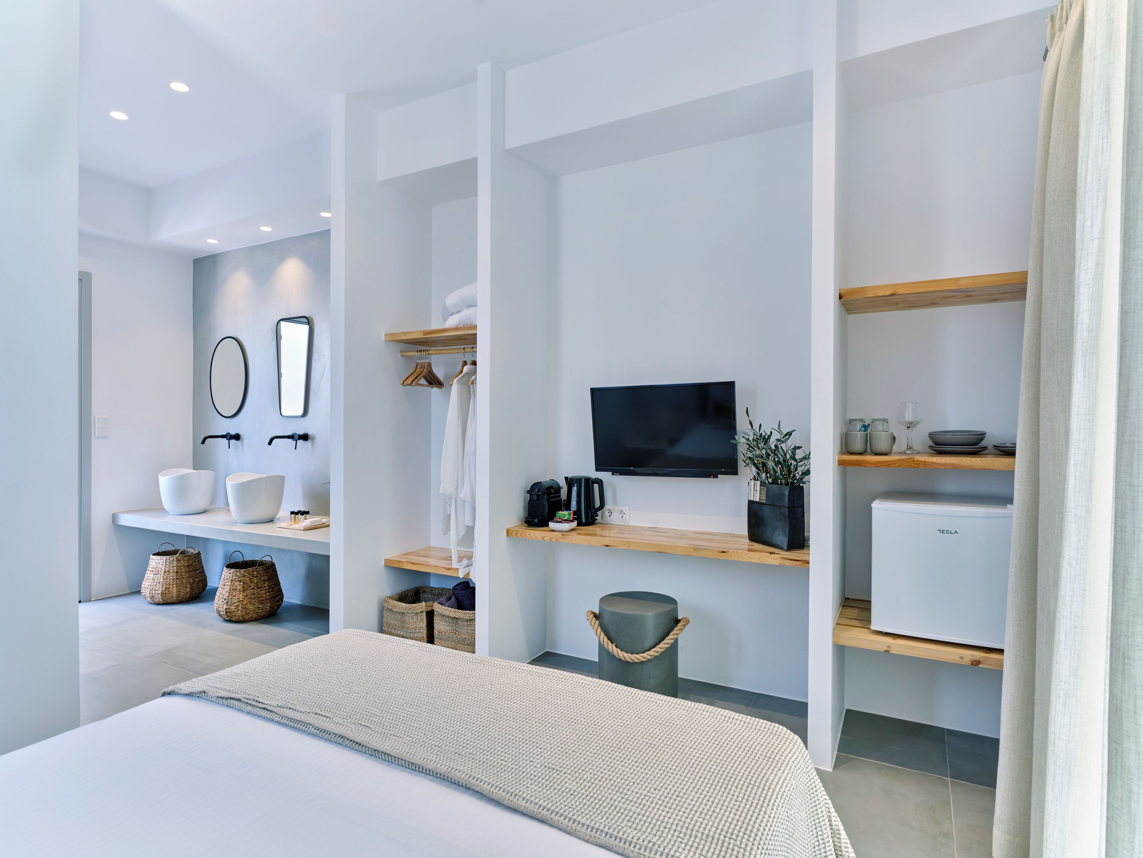 A modern hotel room with a bed, a flat-screen TV, a coffee machine, and a small refrigerator.