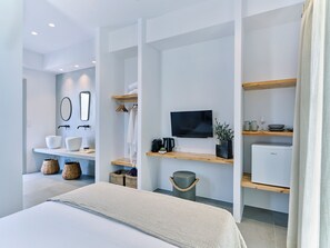A modern hotel room with a bed, a flat-screen TV, a coffee machine, and a small refrigerator. - Blue Mare Villas (Paros)