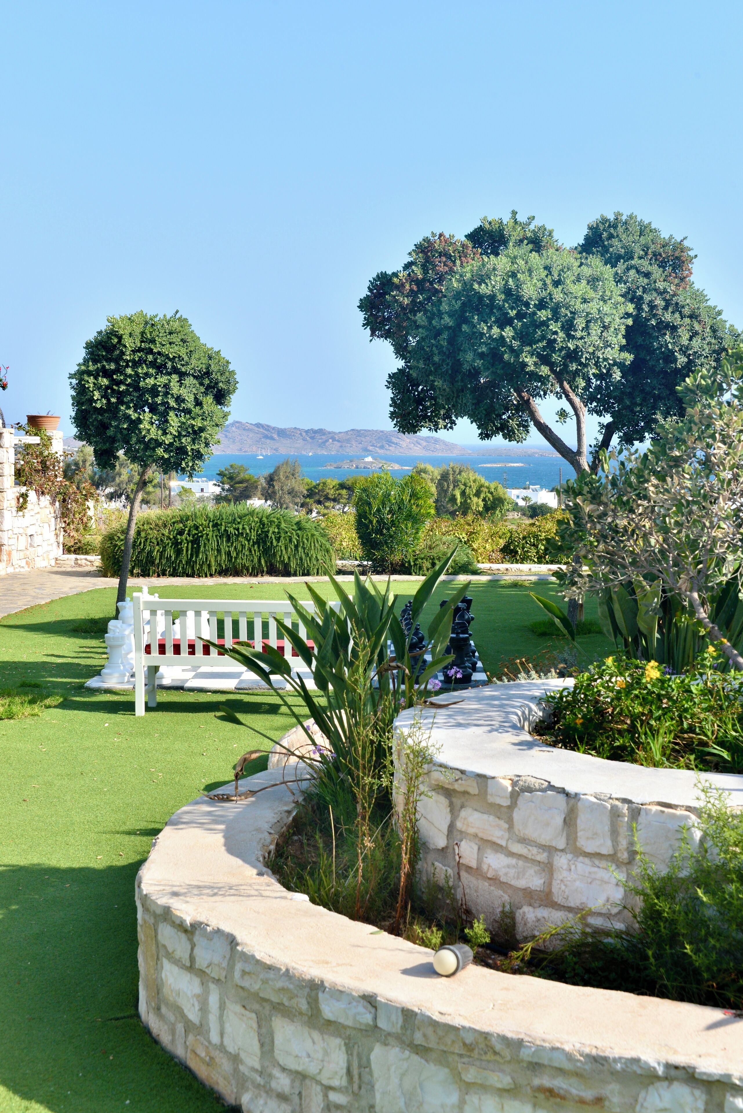 A well-maintained garden with a white bench, stone wall, and a view of the sea.