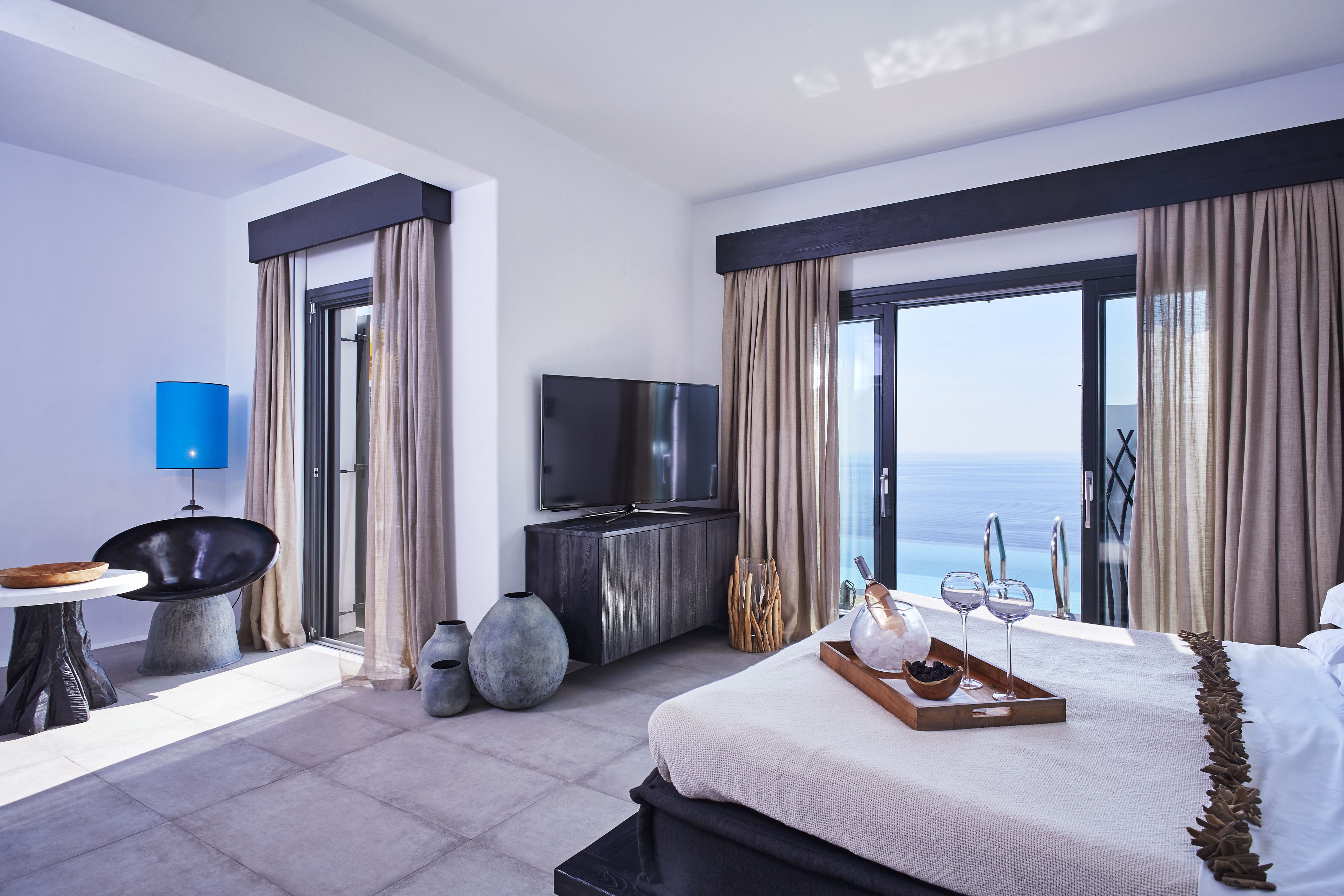 Une chambre d’hôtel moderne dotée d’un grand lit, d’une télévision à écran plat, d’une table à manger et offrant une vue sur la mer.