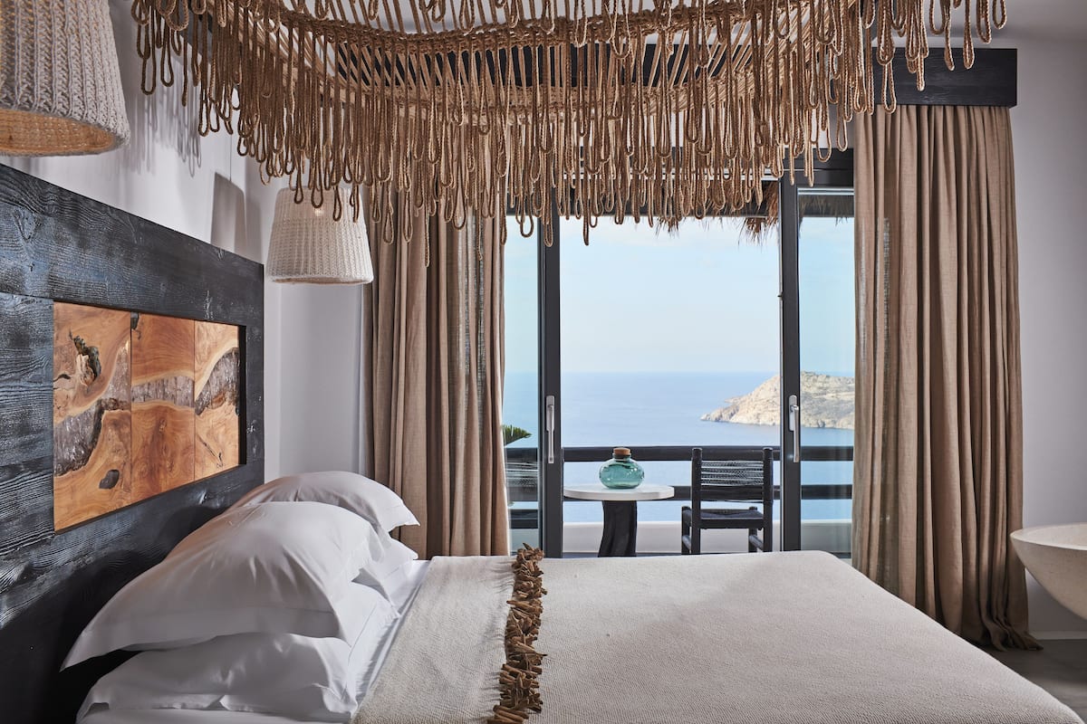 A bedroom with a large bed, a view of the sea, and a painting on the wall.