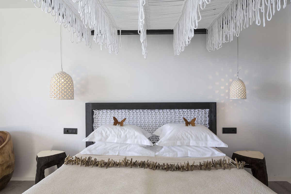 A modern bedroom with a large bed, two hanging pendant lights, and a wooden headboard.