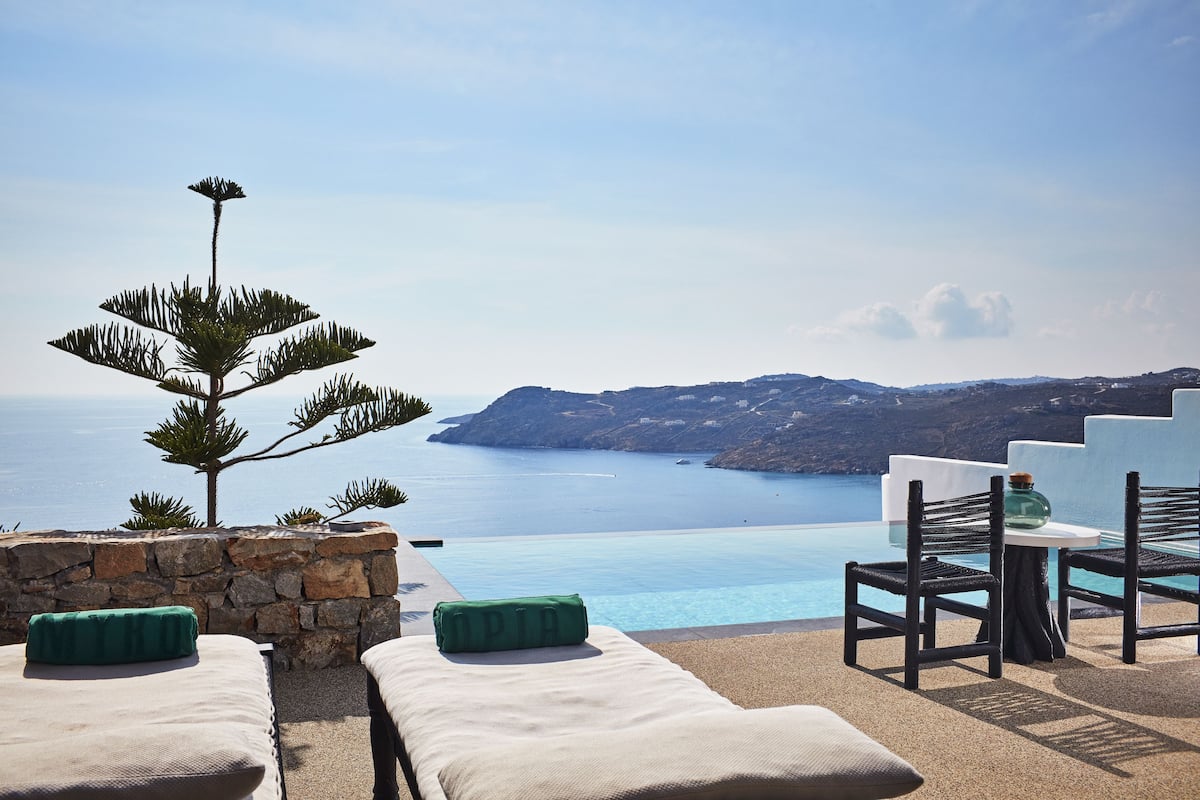 A terrace with a stone wall, a small tree, and a view of the sea.