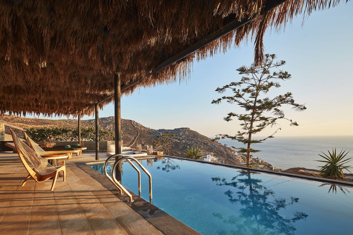 An infinity pool with a view of the ocean, outdoor seating, and a thatched roof structure.