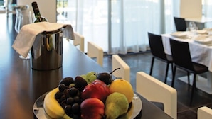Un coin repas avec une table dressée pour deux personnes, un panier de fruits sur la table et une bouteille de vin.