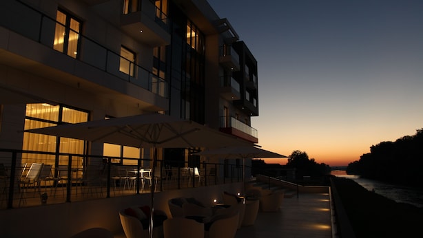 Un hôtel moderne doté d’une terrasse, de grandes fenêtres et offrant une vue sur la rivière au crépuscule.