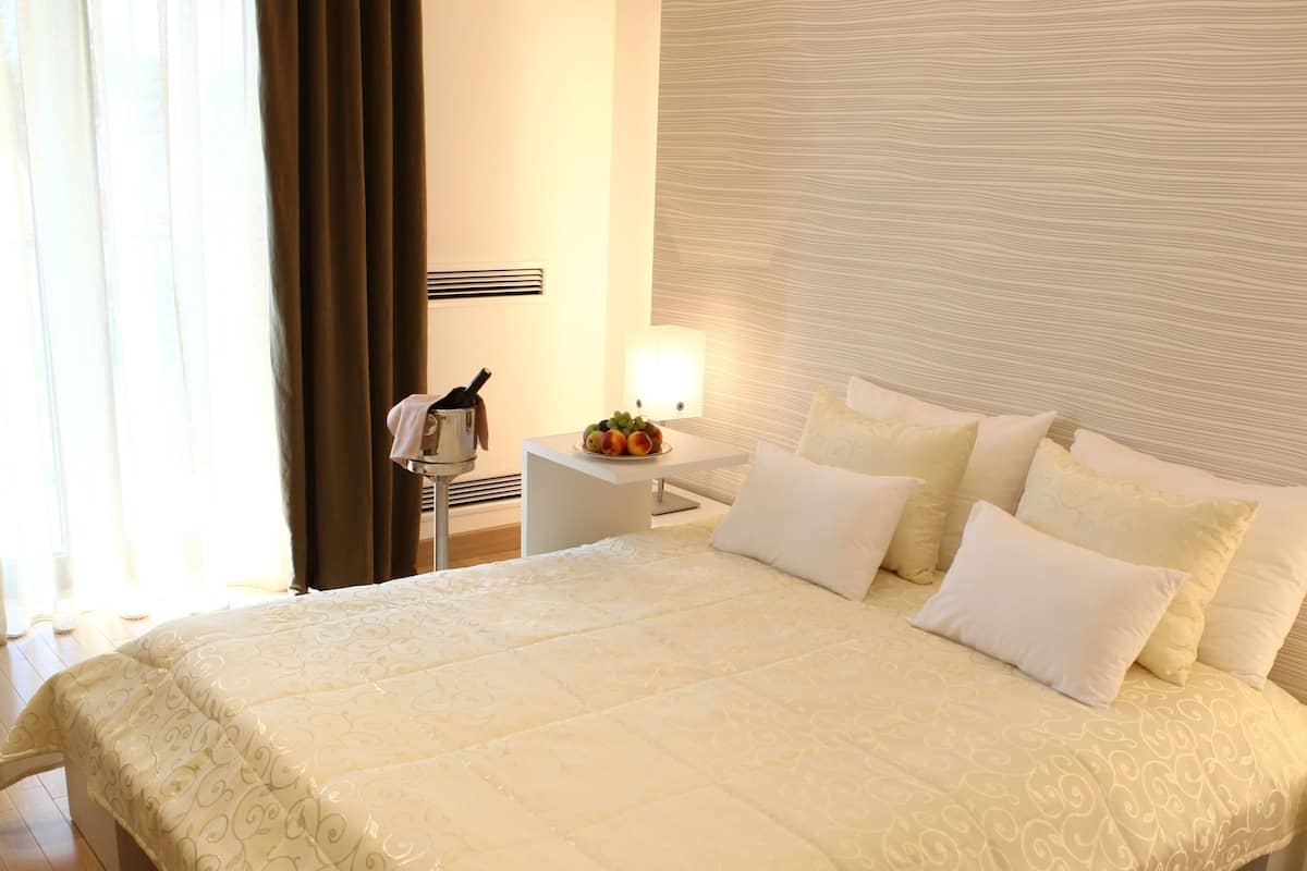 A large bed with a patterned bedspread, a bedside table with a lamp, and a view of the window with curtains.