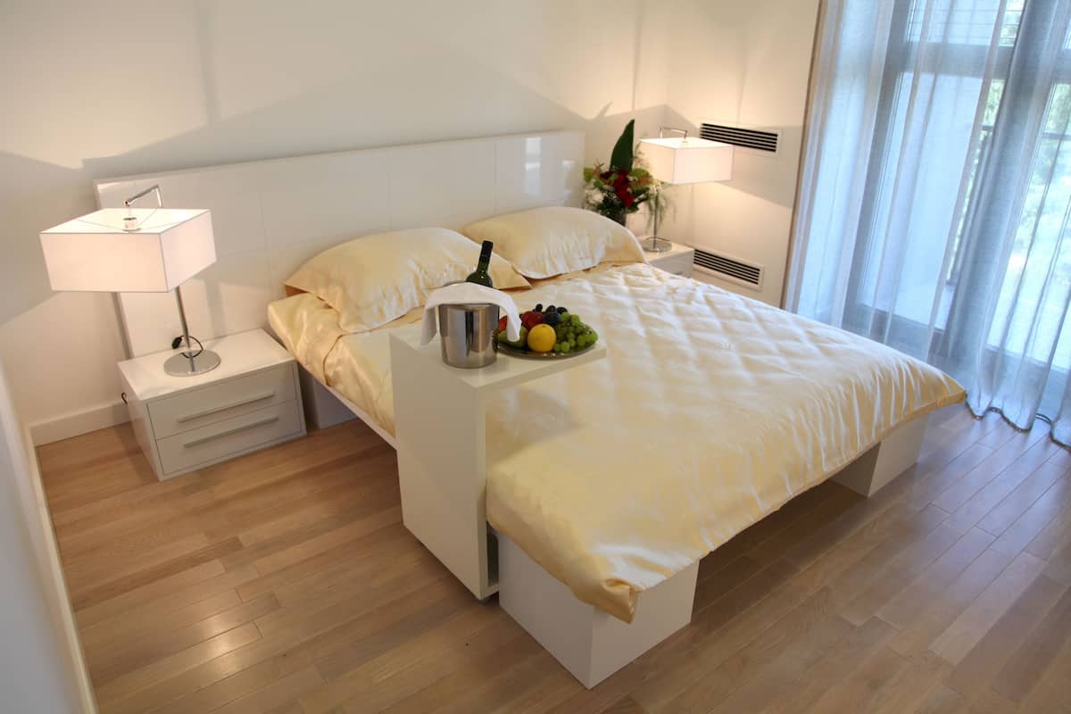 A modern hotel room with a neatly made bed, bedside tables with lamps, a fruit bowl, and a vase with flowers.