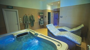 Un espace spa comprenant un bain à remous, deux chaises longues et un porte-serviettes avec des peignoirs.