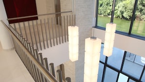 Un intérieur moderne avec un escalier en métal, des rampes en verre et des luminaires suspendus.
