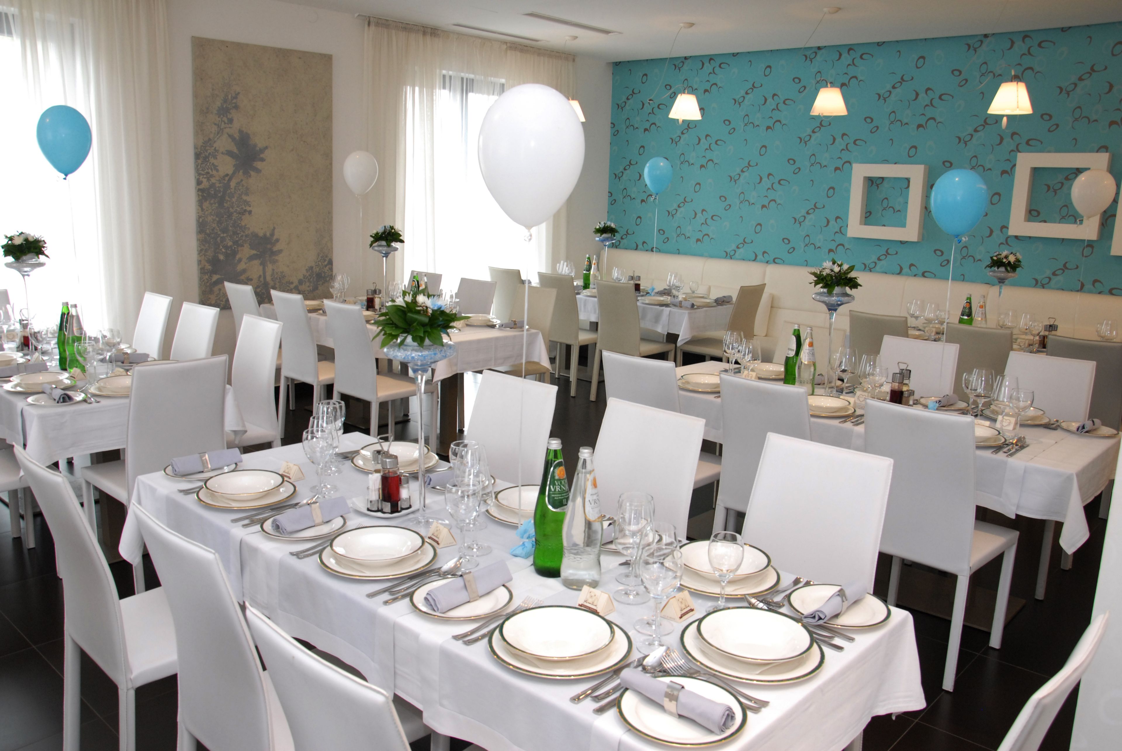 A dining area with multiple tables set for a formal event, featuring white tablecloths, neatly arranged silverware, and glassware.
