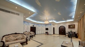 Un lobby espacioso con techo alto, un candelabro, un sofá, una mesita de centro y un televisor.